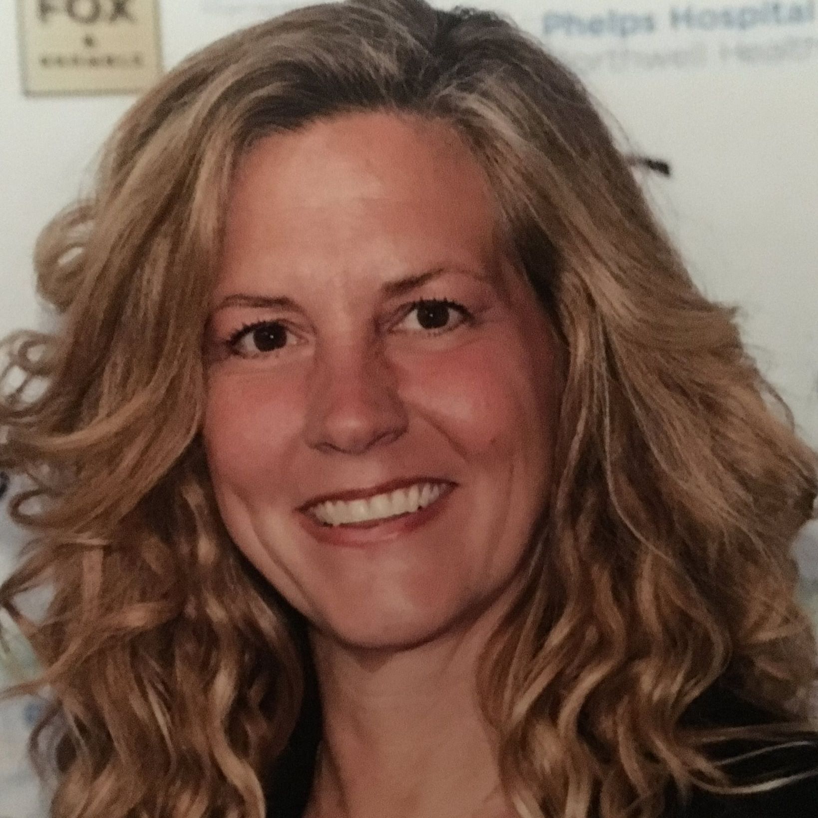 A headshot of a smiling woman with long, wavy blonde hair