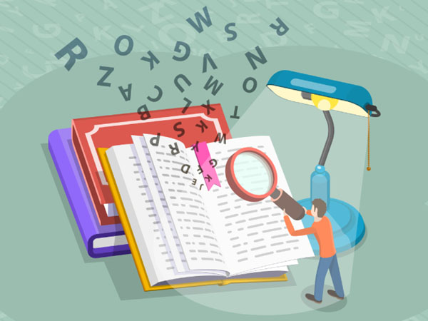 Person using magnifying glass to read an open book beside stacked books and a lamp.