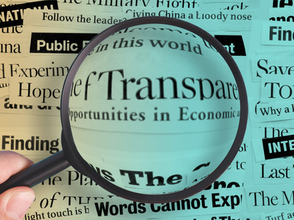 Magnifying glass enlarges word "Transparent" over newspaper text background.