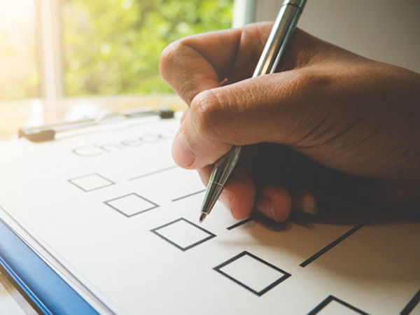 Hand holding pen over checklist with empty boxes.