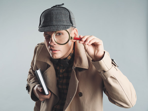 Person in detective costume holding magnifying glass and book.