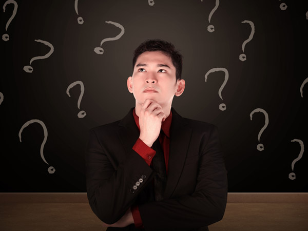 Person thinking with question marks drawn on dark background behind.