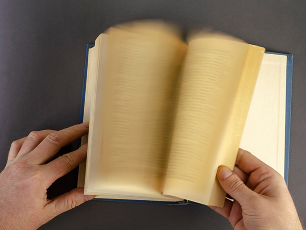 Hands holding open book with blurred pages visible.
