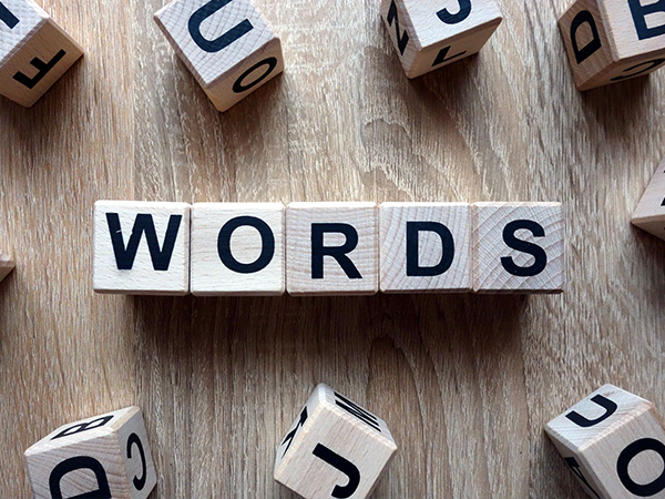 Wooden letter tiles spelling words on wood background, scattered tiles around.