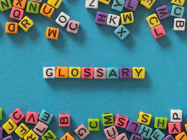 Colorful letter cubes spelling "GLOSSARY" on teal background, surrounded by scattered alphabet cubes.