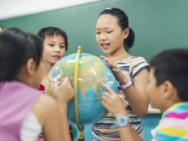 Children gathered around a globe in a classroom, pointing to different places on the map.
