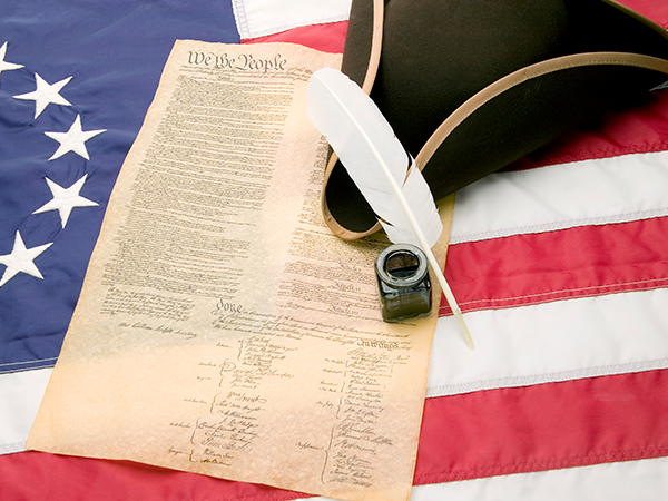 US Constitution with quill pen on American flag background.