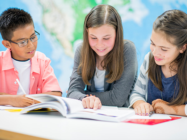 Students studying together reading a book at a table.