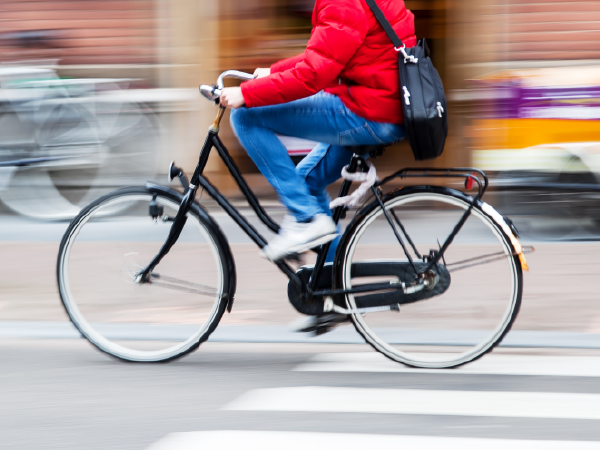 Person in red jacket cycling across street, motion blur.