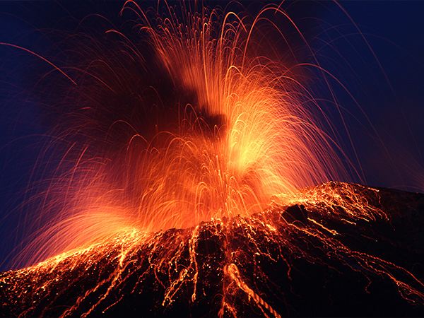 Volcanic eruption with glowing lava and fiery sparks against dark sky.