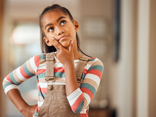 Young girl in striped shirt and overalls looking thoughtful with hand on chin.