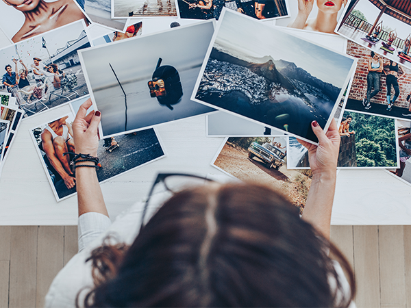 Person sorting through a collection of printed photographs on table.