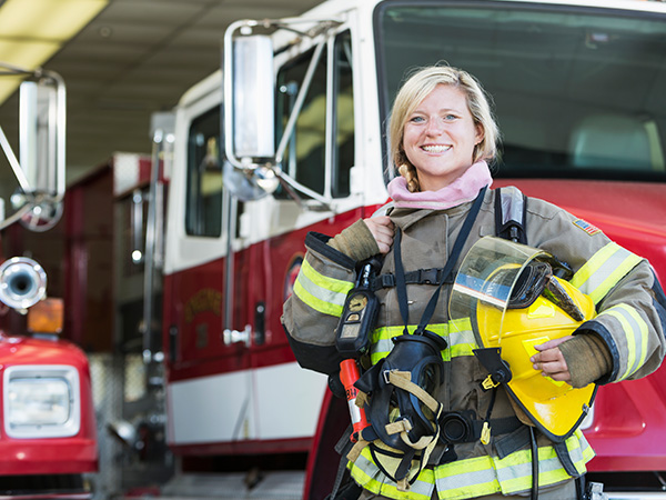 Female firefighter smiling in front of fire truck, holding helmet