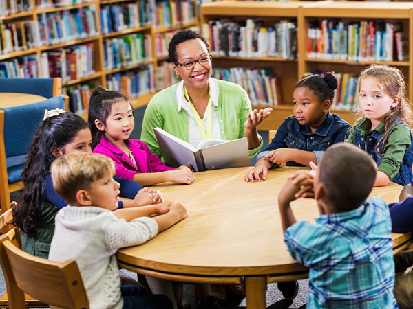 Teacher reading to a group of children in library setting.