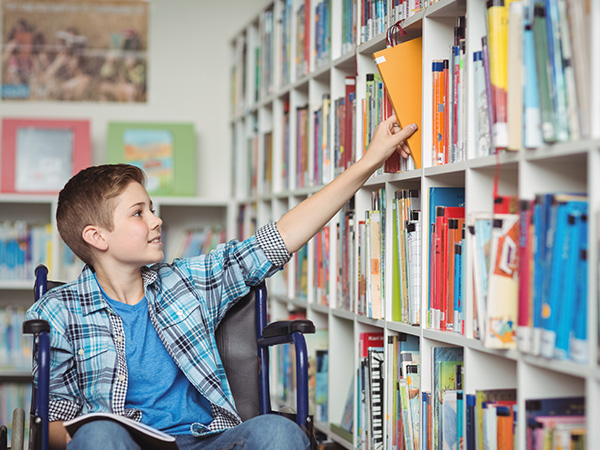 Boy reaching for book on library shelf.