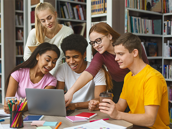 Students smiling while studying together with laptop in library.