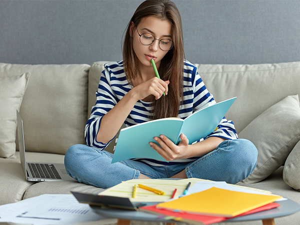 Woman studying on couch with notebook and colored pencils.