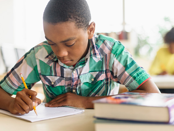 Young person writing in notebook, wearing plaid shirt, focused on work.