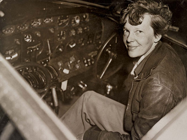 Black and white photo of woman seated in airplane cockpit smiling at camera.
