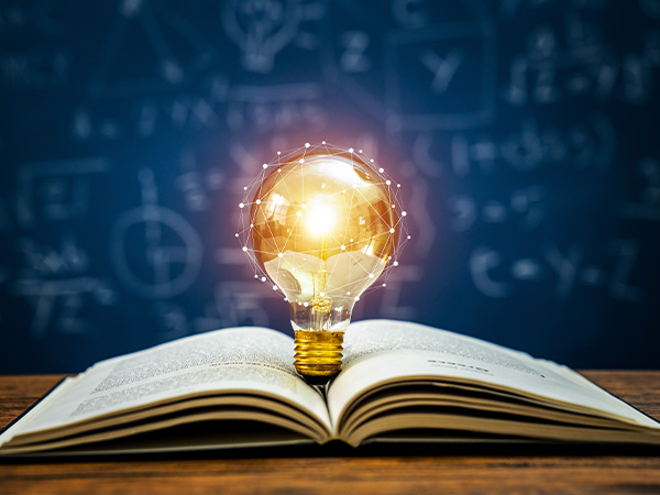 Glowing light bulb on open book, symbols floating in background.